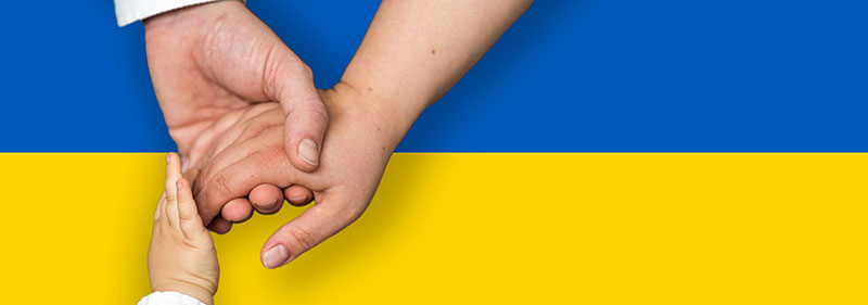 Kinderhände greifen einander vor der Ukrainische Flagge.